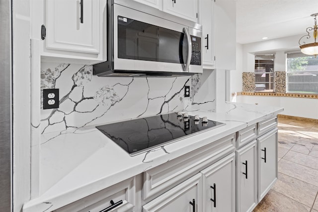 kitchen with black cooktop, hanging light fixtures, tasteful backsplash, light stone counters, and white cabinetry