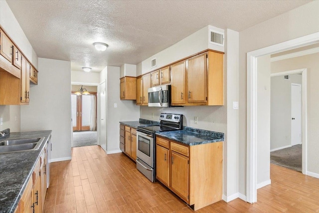 kitchen featuring sink, stainless steel appliances, a textured ceiling, and light wood-type flooring