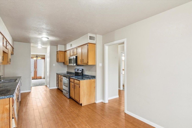 kitchen with appliances with stainless steel finishes, light hardwood / wood-style floors, sink, and a textured ceiling