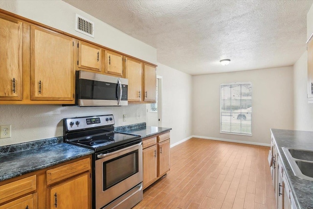 kitchen featuring stainless steel appliances, light hardwood / wood-style floors, and a textured ceiling