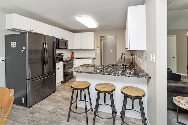 kitchen featuring stainless steel appliances, kitchen peninsula, dark stone counters, decorative backsplash, and white cabinetry