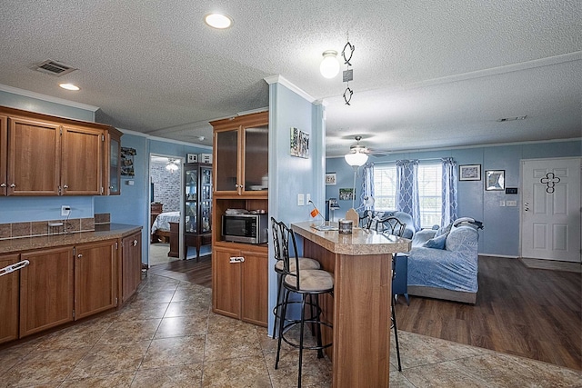 kitchen with a kitchen bar, a textured ceiling, ceiling fan, crown molding, and tile patterned flooring