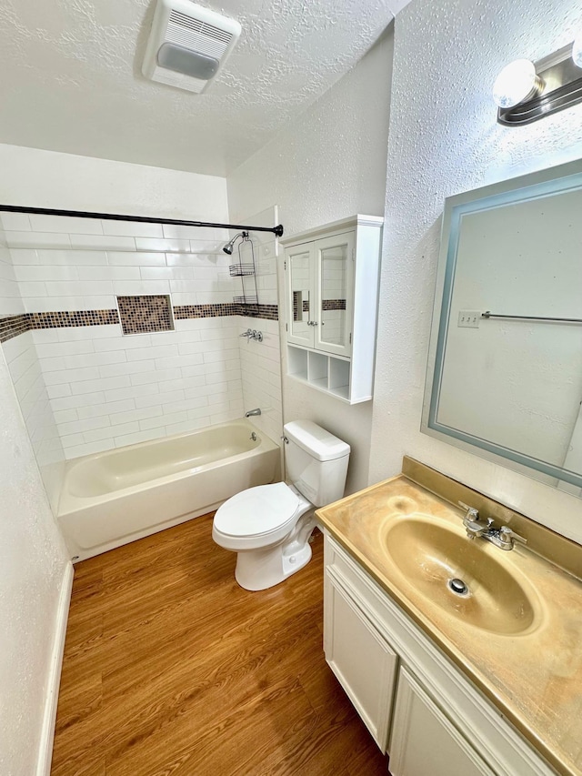 full bathroom with hardwood / wood-style floors, a textured ceiling, toilet, vanity, and tiled shower / bath