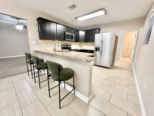 kitchen with dark cabinetry, visible vents, a peninsula, a sink, and stainless steel appliances