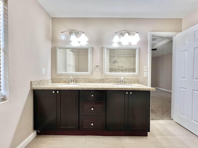 full bathroom with double vanity, walk in shower, baseboards, and a sink