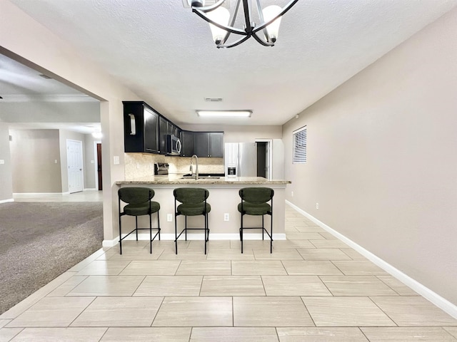 kitchen featuring dark cabinets, a breakfast bar, decorative backsplash, appliances with stainless steel finishes, and a sink