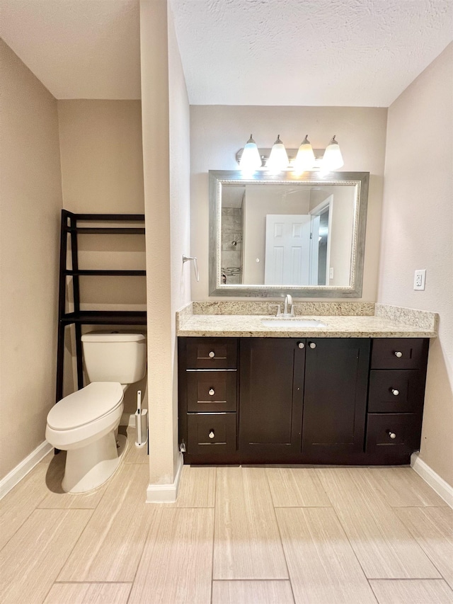 bathroom with vanity, baseboards, walk in shower, a textured ceiling, and toilet