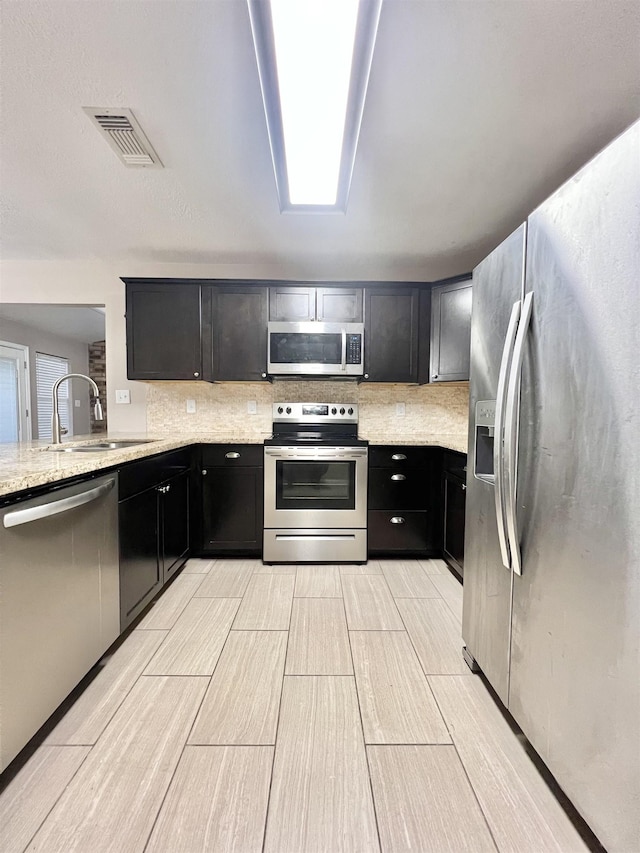 kitchen featuring visible vents, a sink, light stone counters, dark cabinetry, and stainless steel appliances