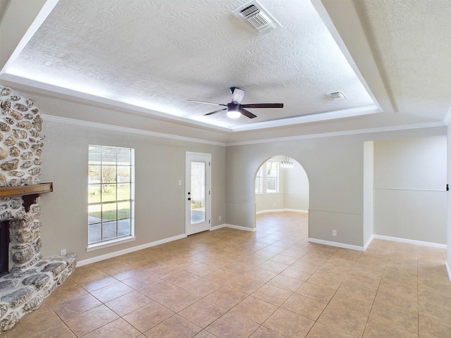 unfurnished living room featuring a raised ceiling, a stone fireplace, ceiling fan, ornamental molding, and light tile patterned flooring