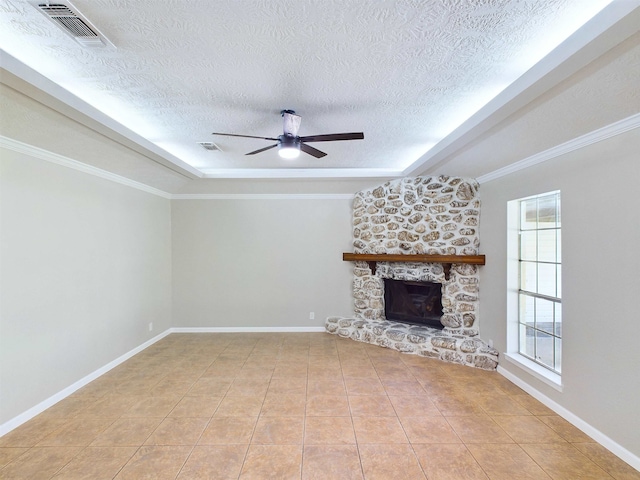 unfurnished living room with ornamental molding, a textured ceiling, ceiling fan, a stone fireplace, and light tile patterned flooring