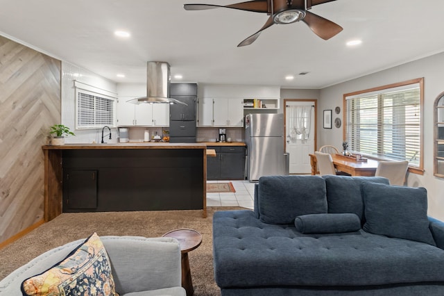 tiled living room with ceiling fan, ornamental molding, sink, and wooden walls