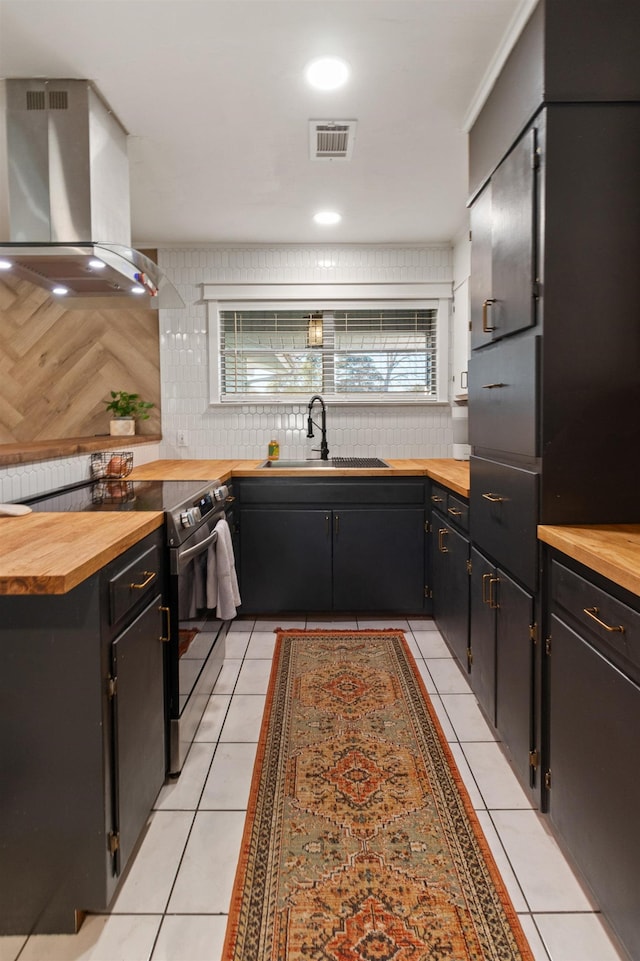 kitchen with sink, wall chimney exhaust hood, wooden counters, stainless steel electric range, and light tile patterned floors