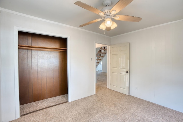 unfurnished bedroom featuring a closet, ornamental molding, a ceiling fan, wood walls, and carpet flooring