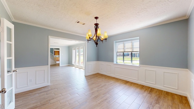 unfurnished room featuring a chandelier, a textured ceiling, a wainscoted wall, light wood-style floors, and ornamental molding
