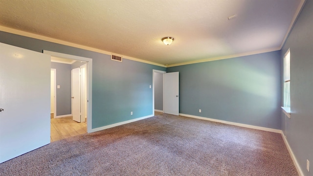 empty room featuring carpet floors, baseboards, a textured ceiling, and crown molding