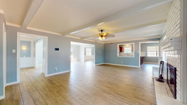 unfurnished living room featuring a textured ceiling, baseboards, beamed ceiling, a brick fireplace, and plenty of natural light