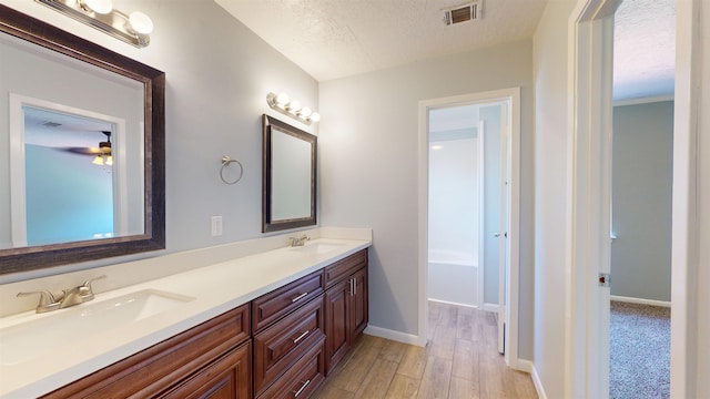 full bath with wood finished floors, a textured ceiling, baseboards, double vanity, and a tub