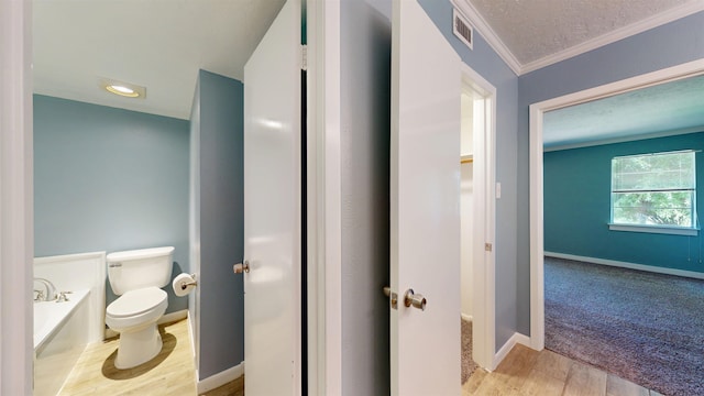 bathroom featuring toilet, a bath, ornamental molding, wood finished floors, and baseboards