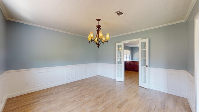 empty room with a chandelier, light wood finished floors, wainscoting, crown molding, and a decorative wall