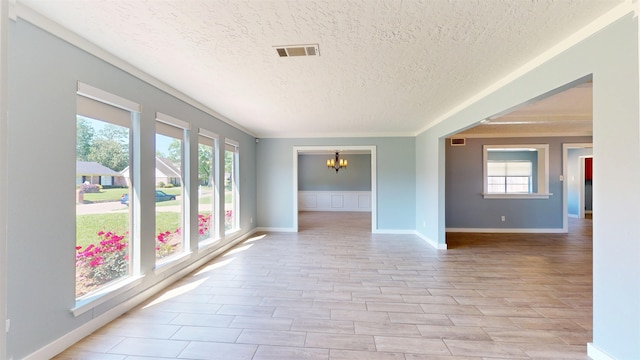 spare room with a textured ceiling, a chandelier, healthy amount of natural light, and baseboards