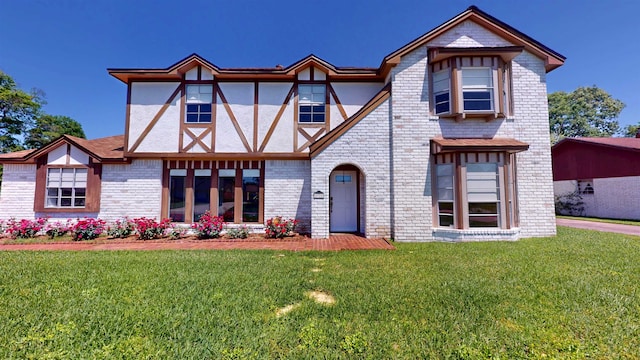 tudor home with a front lawn, brick siding, and stucco siding
