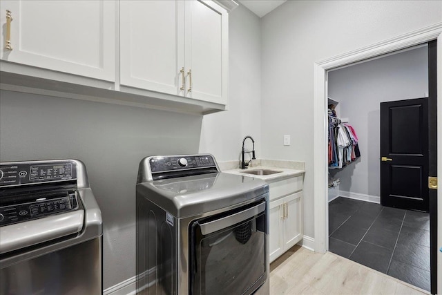 laundry room featuring wood finished floors, a sink, baseboards, cabinet space, and washer and clothes dryer