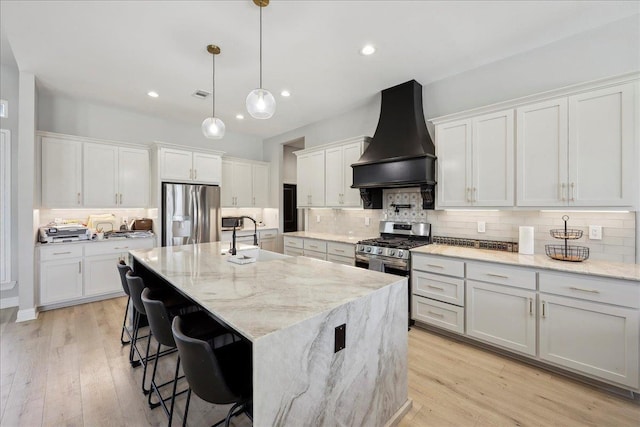 kitchen with light wood-style flooring, a sink, appliances with stainless steel finishes, custom exhaust hood, and tasteful backsplash