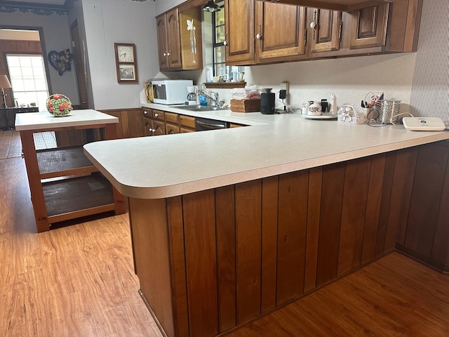 kitchen with stainless steel dishwasher, kitchen peninsula, sink, and light hardwood / wood-style flooring