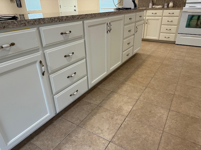 kitchen with dark stone countertops, white cabinets, light tile patterned floors, and range