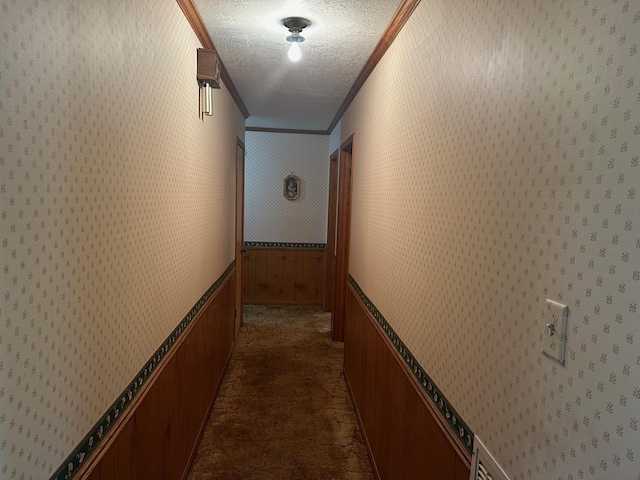 corridor with crown molding, wood walls, dark carpet, and a textured ceiling