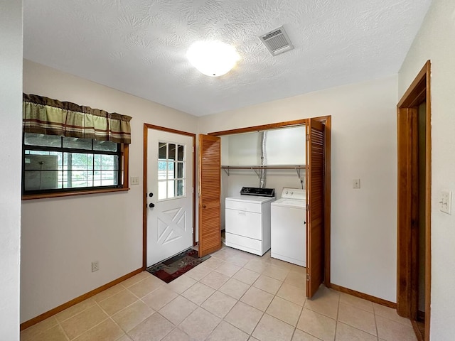 laundry area featuring washing machine and dryer, light tile patterned floors, and a textured ceiling