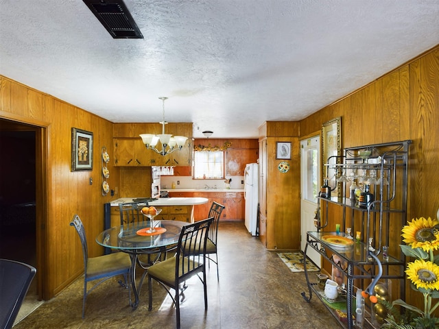 dining area with a textured ceiling, wooden walls, a notable chandelier, and sink