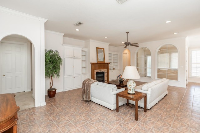 living room with arched walkways, visible vents, a ceiling fan, ornamental molding, and a glass covered fireplace