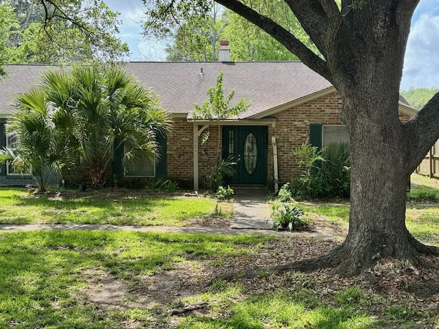 ranch-style home with brick siding, a front yard, a shingled roof, and a chimney
