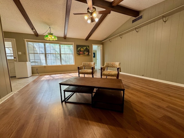 living area featuring lofted ceiling with beams, a textured ceiling, visible vents, wood finished floors, and ceiling fan