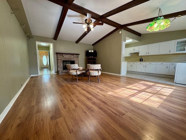 living area featuring lofted ceiling with beams, light wood-style flooring, baseboards, ceiling fan, and a fireplace