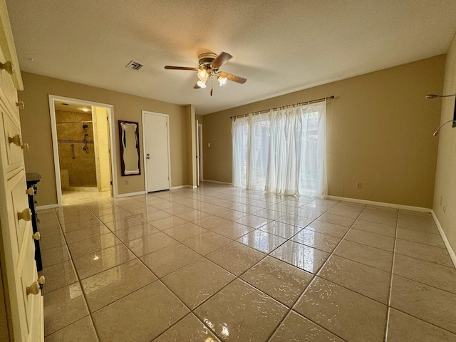 empty room with tile patterned floors, visible vents, a ceiling fan, baseboards, and a textured ceiling