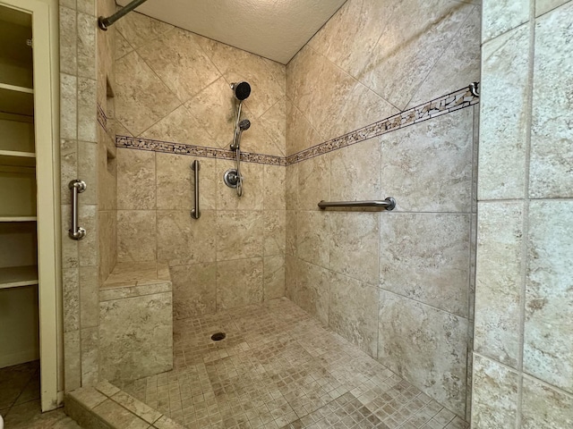 bathroom with a tile shower, a spacious closet, and a textured ceiling