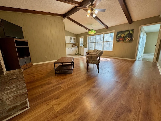 living area with wood finished floors, a textured ceiling, vaulted ceiling with beams, ceiling fan, and baseboards