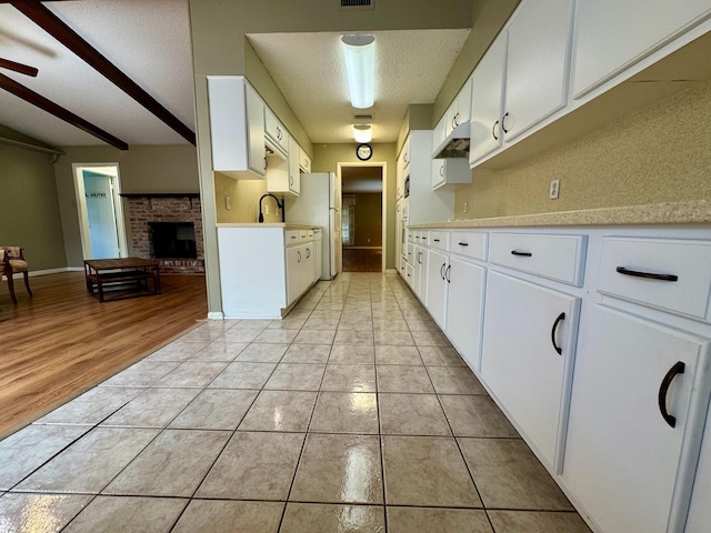 kitchen with a textured ceiling, a sink, light tile patterned floors, light countertops, and freestanding refrigerator