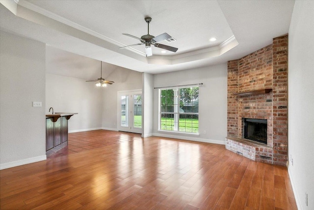 unfurnished living room featuring ornamental molding, a tray ceiling, wood finished floors, a fireplace, and baseboards