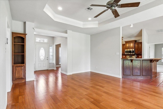 unfurnished living room featuring a raised ceiling, light wood-style flooring, visible vents, and ornamental molding