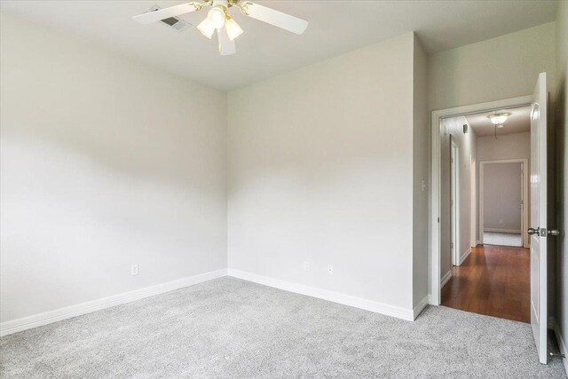 carpeted empty room with visible vents, ceiling fan, attic access, and baseboards