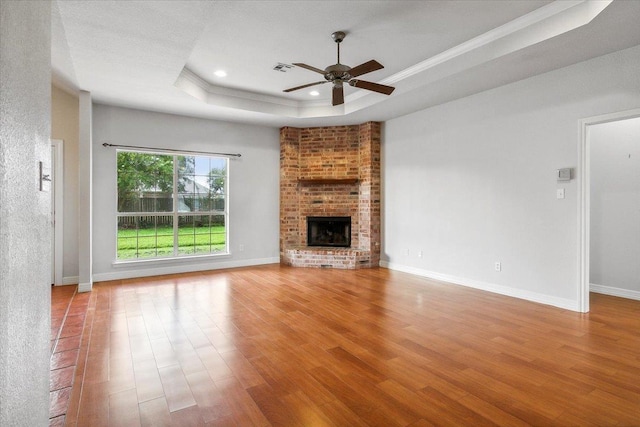 unfurnished living room with a tray ceiling, a brick fireplace, wood finished floors, and baseboards