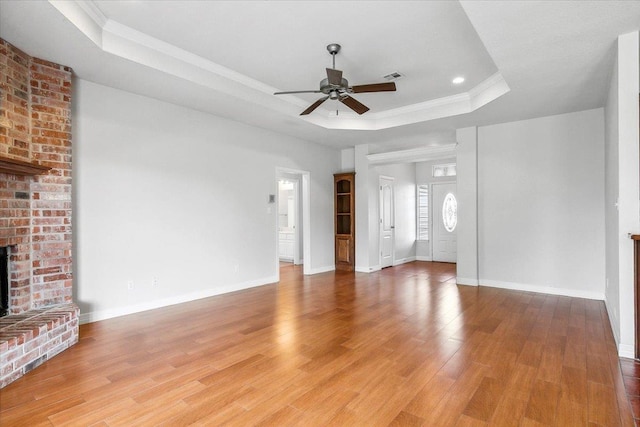 unfurnished living room with visible vents, a brick fireplace, crown molding, a tray ceiling, and light wood-style flooring