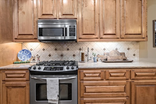 kitchen with light stone counters, appliances with stainless steel finishes, and backsplash