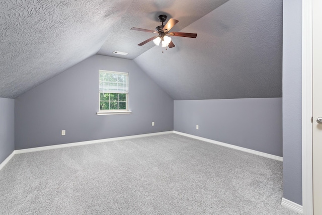 additional living space with a textured ceiling, carpet, baseboards, vaulted ceiling, and visible vents