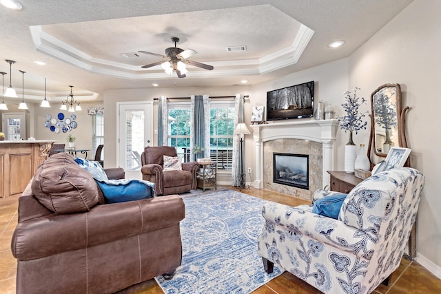 living area featuring a high end fireplace, a raised ceiling, ceiling fan with notable chandelier, and visible vents