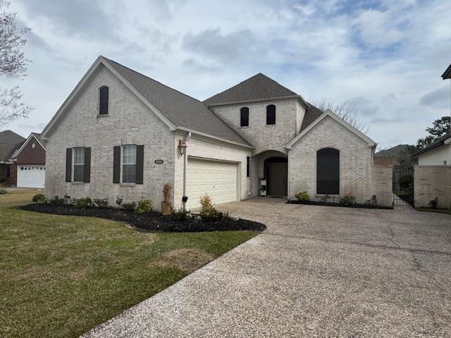 french country style house featuring a garage, a front yard, brick siding, and driveway