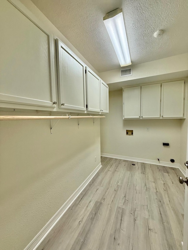 clothes washing area with visible vents, gas dryer hookup, light wood finished floors, baseboards, and cabinet space